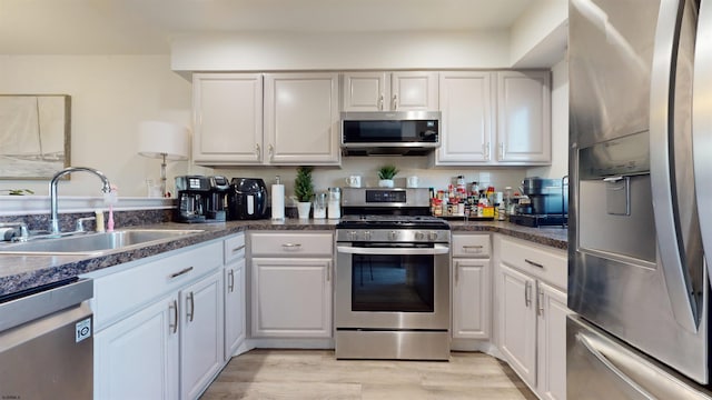 kitchen with appliances with stainless steel finishes, light hardwood / wood-style floors, sink, and white cabinets