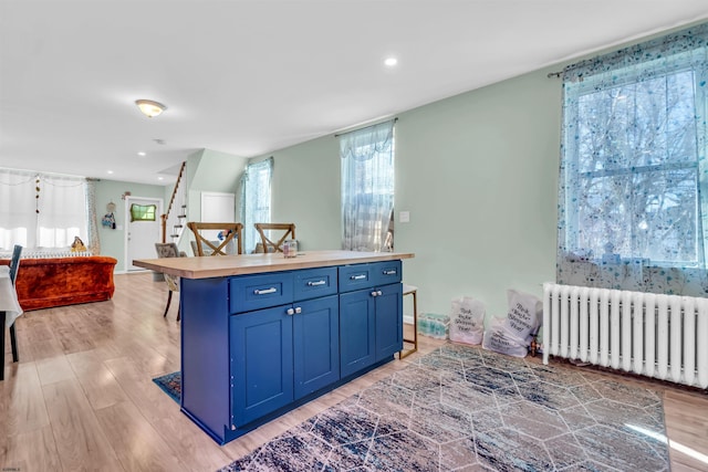 kitchen featuring radiator, blue cabinetry, a breakfast bar, a center island, and light hardwood / wood-style floors