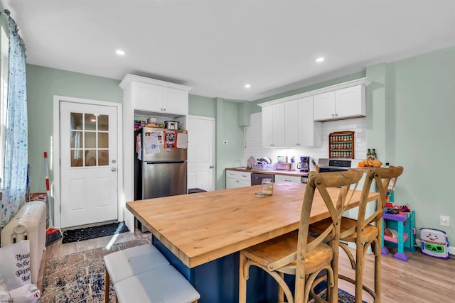 kitchen with backsplash, light hardwood / wood-style floors, stainless steel refrigerator, and white cabinets