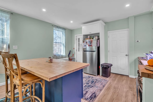 kitchen featuring a breakfast bar area, wooden counters, stainless steel fridge, light hardwood / wood-style floors, and white cabinets