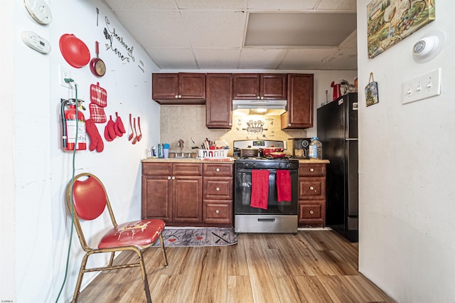 kitchen with a paneled ceiling, wood-type flooring, backsplash, stainless steel gas range oven, and black fridge