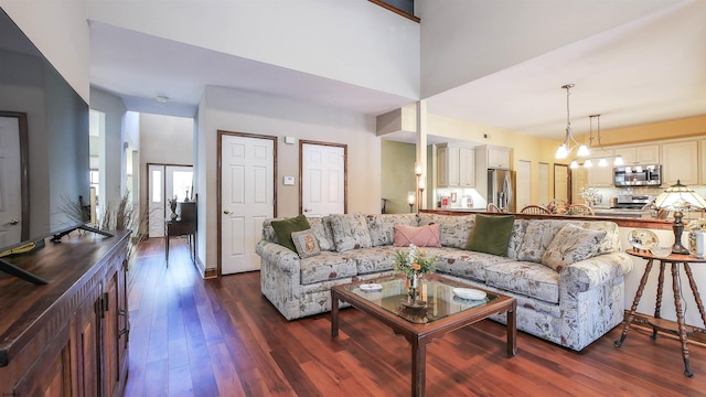 living room with a high ceiling, a notable chandelier, and dark hardwood / wood-style flooring