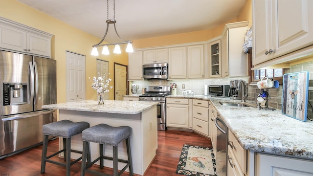 kitchen featuring light stone counters, a center island, hanging light fixtures, stainless steel appliances, and backsplash