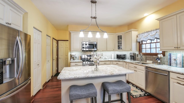 kitchen with a breakfast bar, light stone counters, decorative light fixtures, a center island, and appliances with stainless steel finishes