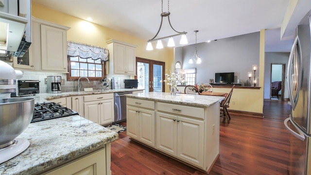 kitchen featuring appliances with stainless steel finishes, a center island, light stone countertops, decorative backsplash, and decorative light fixtures