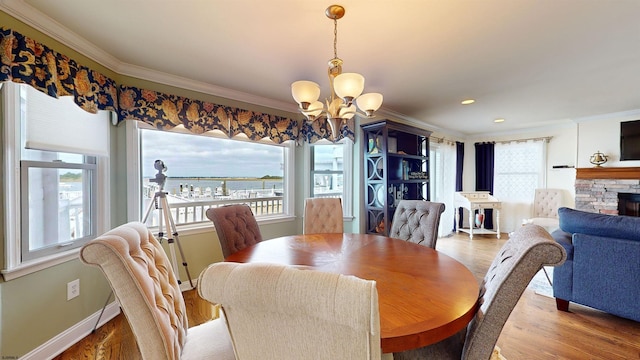 dining space featuring a stone fireplace, hardwood / wood-style floors, a notable chandelier, crown molding, and a water view