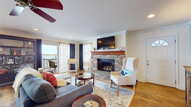 living room with ceiling fan, ornamental molding, a fireplace, and light hardwood / wood-style floors