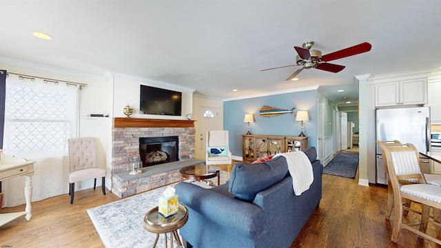 living room with crown molding, a stone fireplace, wood-type flooring, and ceiling fan