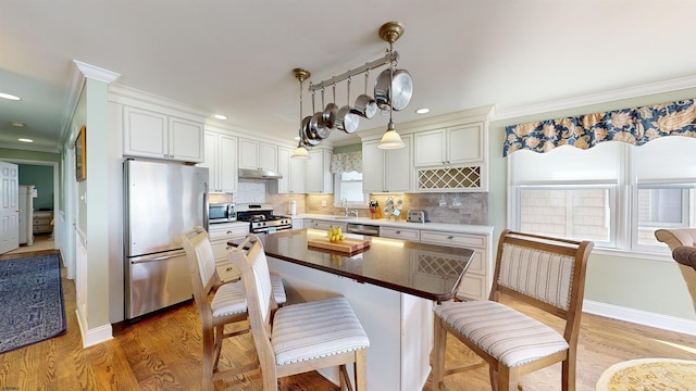 kitchen featuring crown molding, appliances with stainless steel finishes, hanging light fixtures, a kitchen island, and decorative backsplash