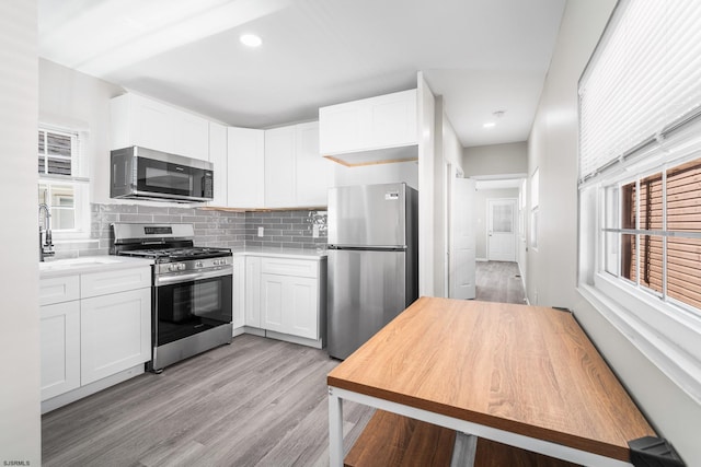 kitchen featuring white cabinets, decorative backsplash, stainless steel appliances, plenty of natural light, and light wood-type flooring