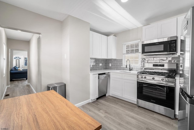 kitchen with sink, white cabinetry, stainless steel appliances, light hardwood / wood-style floors, and decorative backsplash