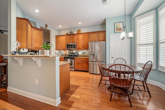 kitchen featuring light hardwood / wood-style flooring, stainless steel appliances, light stone counters, a kitchen bar, and kitchen peninsula