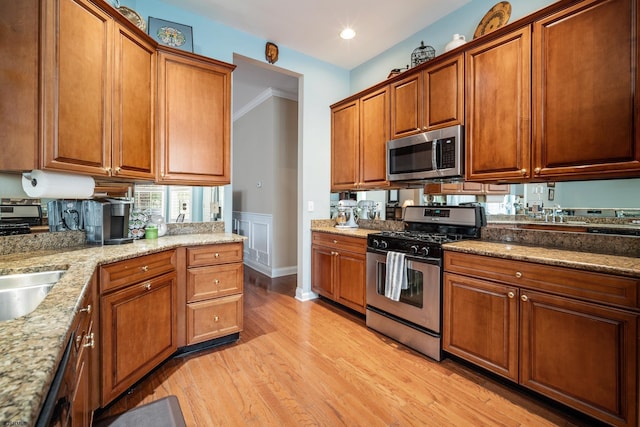 kitchen with sink, crown molding, appliances with stainless steel finishes, light stone countertops, and light wood-type flooring