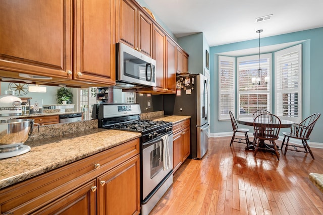 kitchen with pendant lighting, light hardwood / wood-style flooring, appliances with stainless steel finishes, light stone counters, and a chandelier