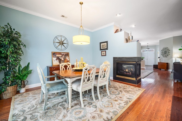 dining area featuring ornamental molding, dark hardwood / wood-style floors, and a multi sided fireplace