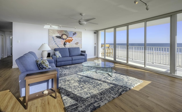 living room with rail lighting, wood-type flooring, a wall of windows, ceiling fan, and a water view