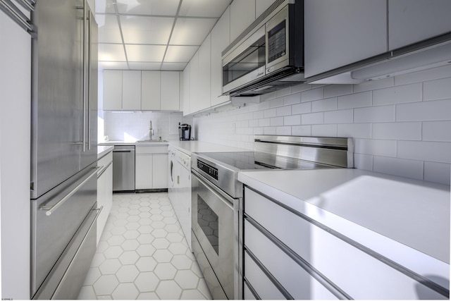 kitchen with sink, tasteful backsplash, light tile patterned floors, stainless steel appliances, and white cabinets