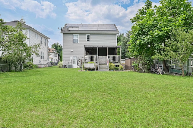 back of property with cooling unit, a yard, and solar panels