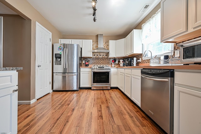 kitchen with appliances with stainless steel finishes, white cabinets, backsplash, and wall chimney exhaust hood