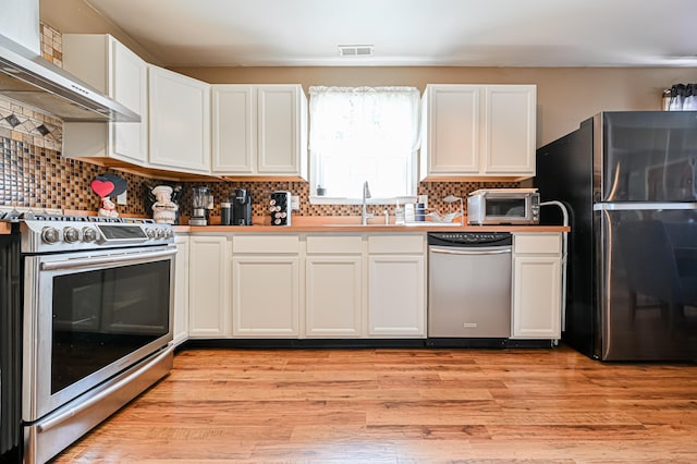 kitchen with white cabinetry, appliances with stainless steel finishes, wall chimney range hood, and light hardwood / wood-style flooring