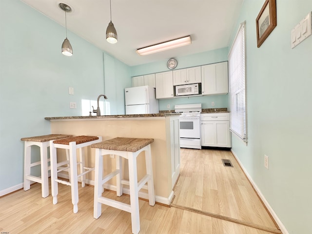 kitchen with a kitchen bar, white cabinetry, light hardwood / wood-style flooring, kitchen peninsula, and white appliances