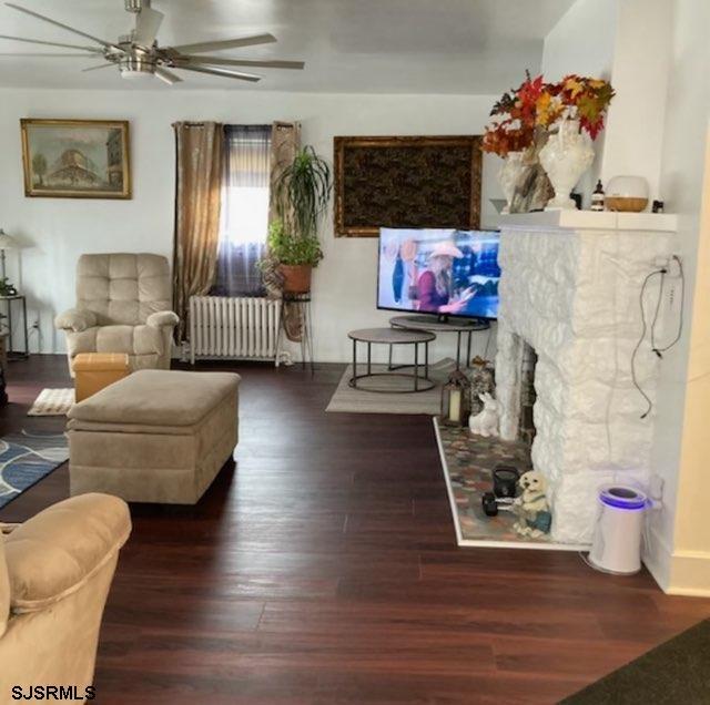 living room with a fireplace, dark wood finished floors, a ceiling fan, and radiator