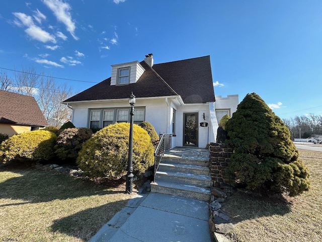 view of front of house featuring a front yard, roof with shingles, a chimney, and stucco siding