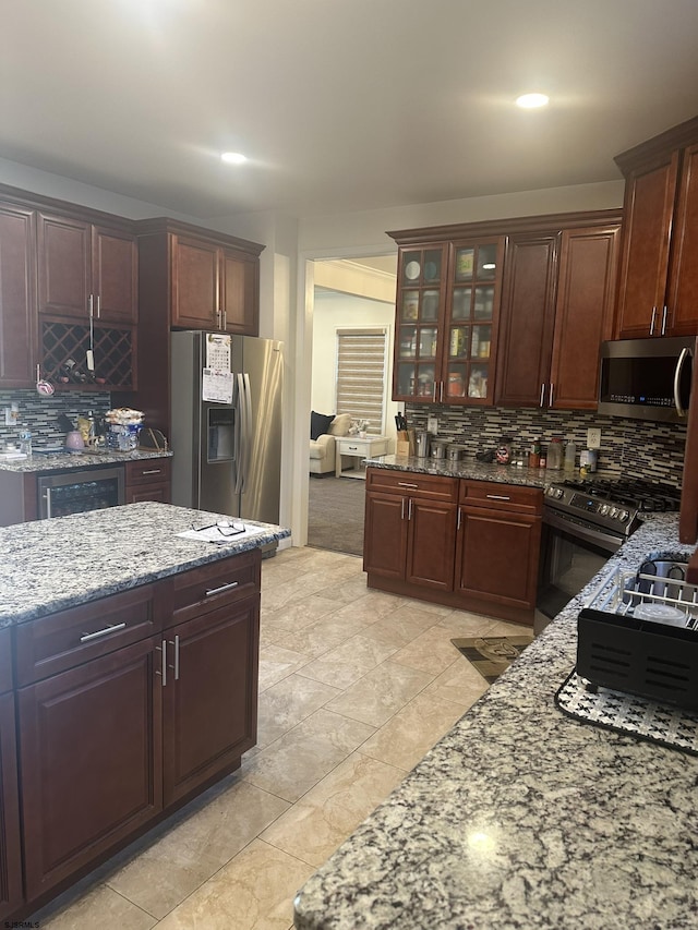 kitchen with stainless steel appliances, tasteful backsplash, light stone countertops, and beverage cooler