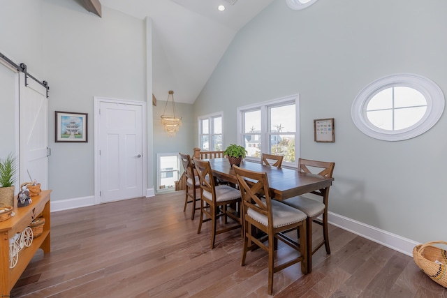 dining area featuring dark hardwood / wood-style flooring, high vaulted ceiling, and a barn door