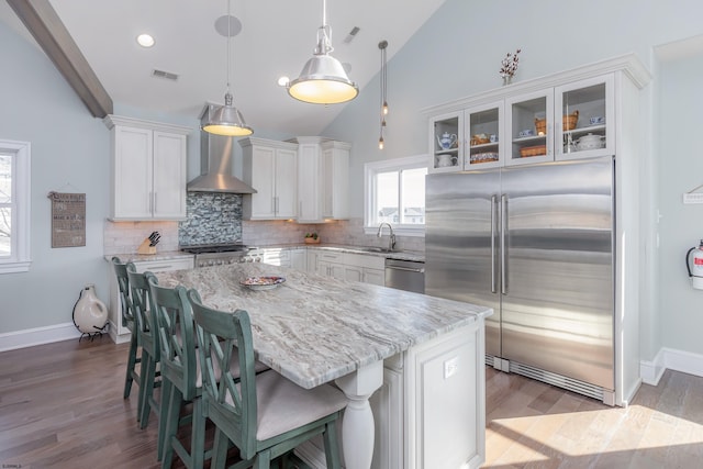 kitchen featuring pendant lighting, white cabinets, a center island, stainless steel appliances, and wall chimney range hood