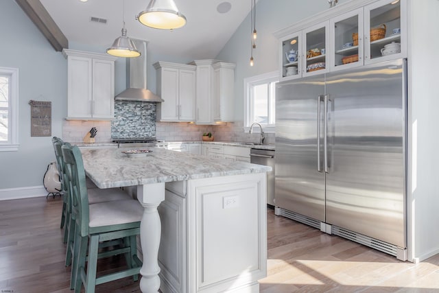 kitchen with wall chimney exhaust hood, a center island, pendant lighting, stainless steel appliances, and white cabinets