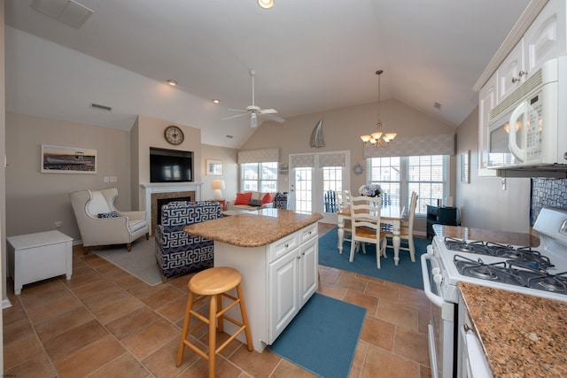 kitchen with pendant lighting, white appliances, white cabinetry, a center island, and vaulted ceiling