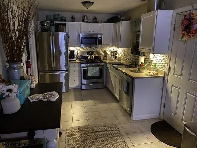 kitchen with white cabinetry, stainless steel appliances, light tile patterned flooring, and tasteful backsplash