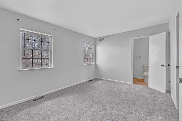 unfurnished bedroom featuring light carpet and ensuite bath