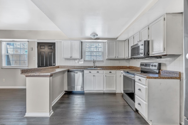 kitchen with appliances with stainless steel finishes, sink, white cabinets, dark hardwood / wood-style flooring, and kitchen peninsula