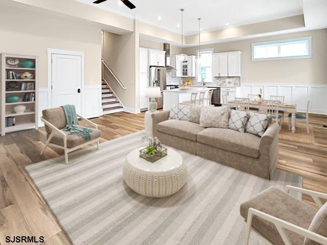 living room featuring a raised ceiling, ceiling fan, and light hardwood / wood-style floors