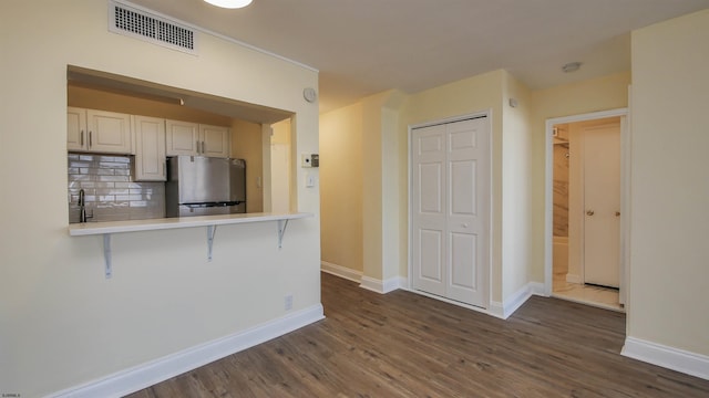 kitchen featuring dark hardwood / wood-style floors, stainless steel fridge, a kitchen bar, decorative backsplash, and kitchen peninsula