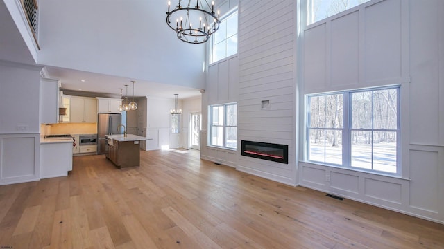 unfurnished living room featuring a towering ceiling, a notable chandelier, light hardwood / wood-style floors, and a fireplace