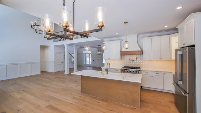 kitchen with white cabinetry, high end appliances, a center island with sink, and decorative light fixtures