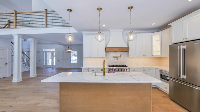 kitchen featuring white cabinetry, light stone counters, premium appliances, a center island with sink, and custom exhaust hood