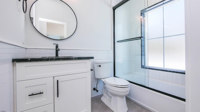 full bathroom featuring combined bath / shower with glass door, tile walls, tile patterned flooring, vanity, and toilet