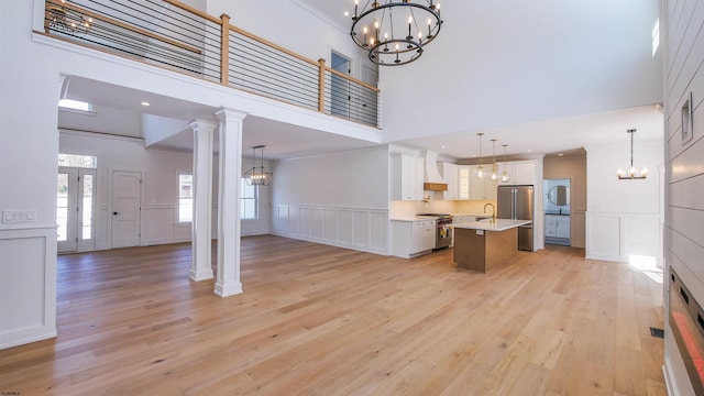 unfurnished living room featuring a notable chandelier, light hardwood / wood-style floors, a high ceiling, and ornate columns