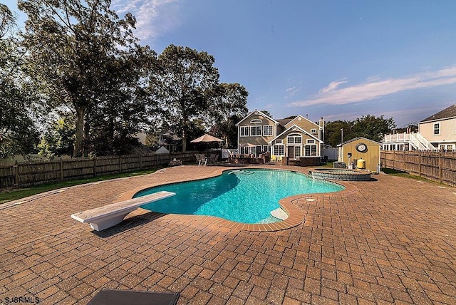 view of swimming pool featuring an in ground hot tub, a storage shed, a diving board, and a patio area