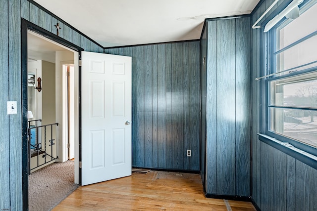 unfurnished bedroom with crown molding, wooden walls, and light wood-type flooring