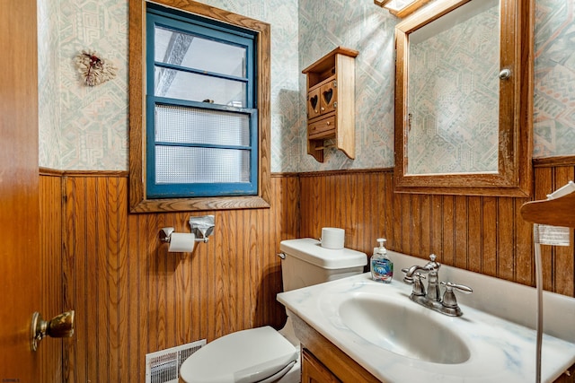 bathroom featuring vanity, wooden walls, and toilet