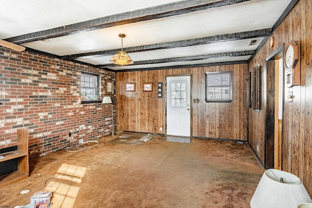 foyer entrance with wood walls, a textured ceiling, carpet floors, brick wall, and beam ceiling