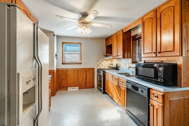 kitchen featuring ceiling fan, wooden walls, sink, and black appliances