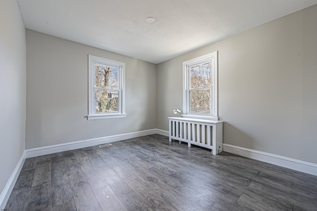 unfurnished room with plenty of natural light, dark hardwood / wood-style floors, and radiator heating unit