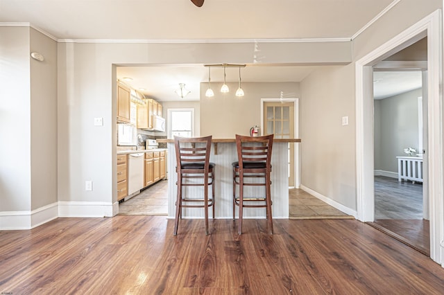 kitchen featuring crown molding, decorative light fixtures, a kitchen breakfast bar, dishwasher, and light hardwood / wood-style floors