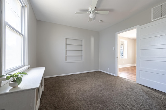 empty room featuring dark colored carpet, built in features, and ceiling fan